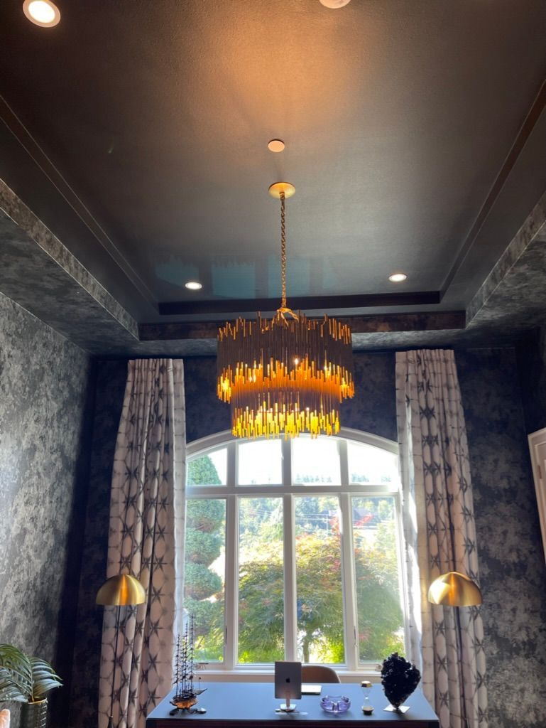 Elegant room with chandelier, window, dark walls and ceiling, two gold sconces, and curtains.