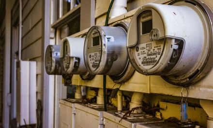 Row of utility meters mounted on the side of a building, beige, with attached white conduit pipes.