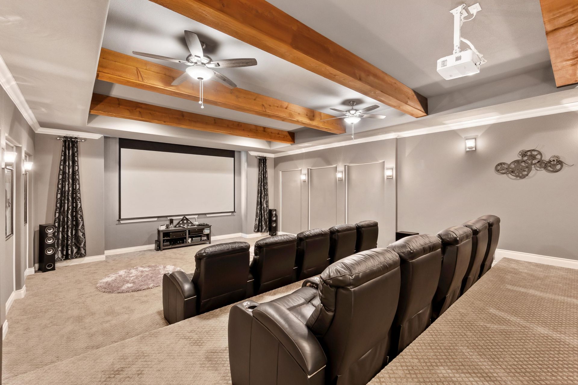 Home theater with rows of black recliners, screen, projector, and exposed wood beams.