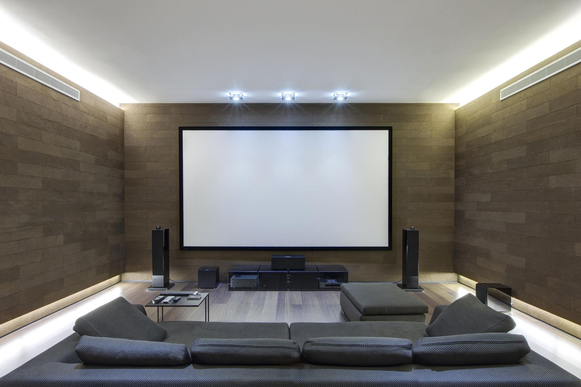 Modern home theater with a large screen, speakers, and a sectional sofa.