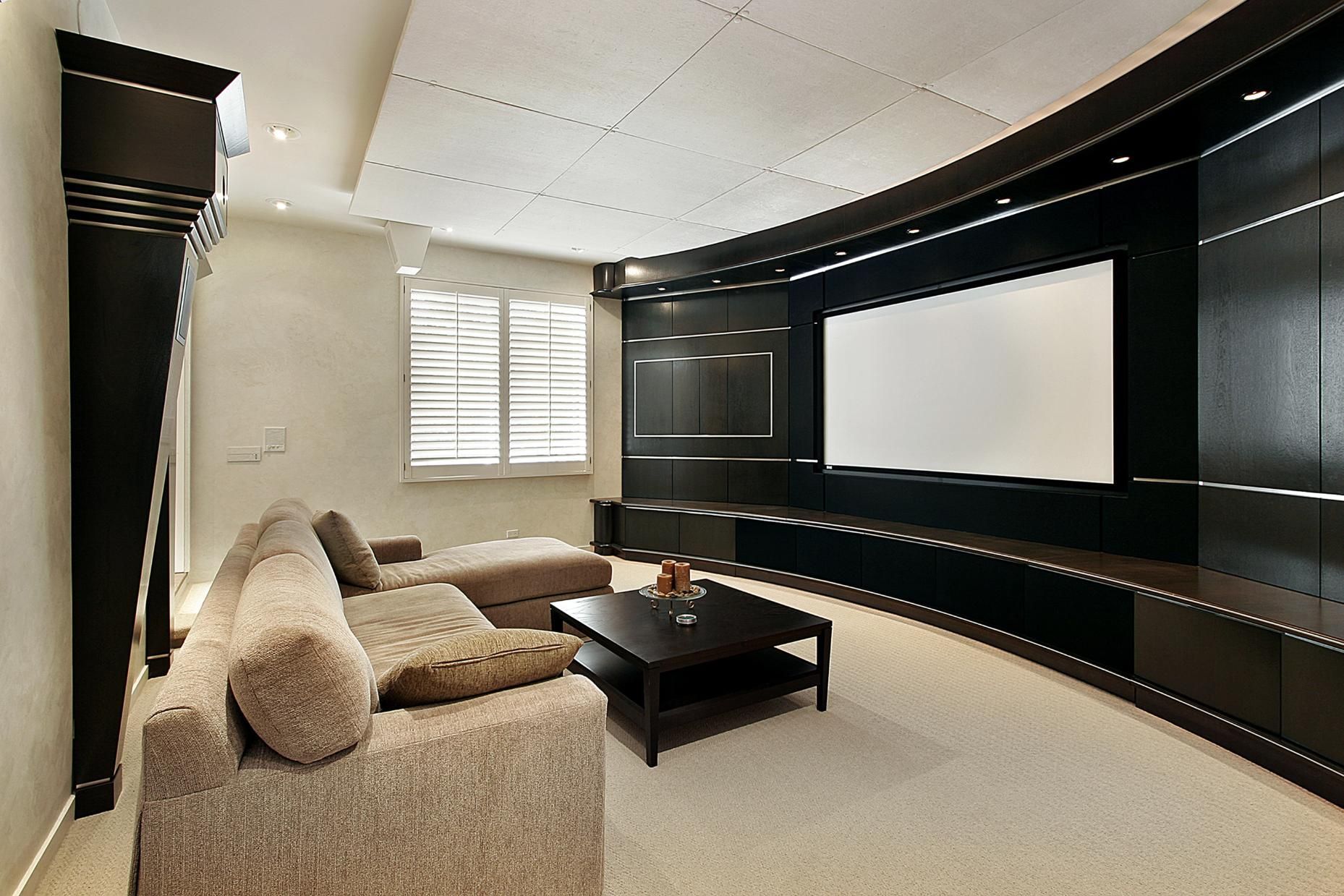Home theater with a curved black wall and large screen, beige sofa, and low coffee table.