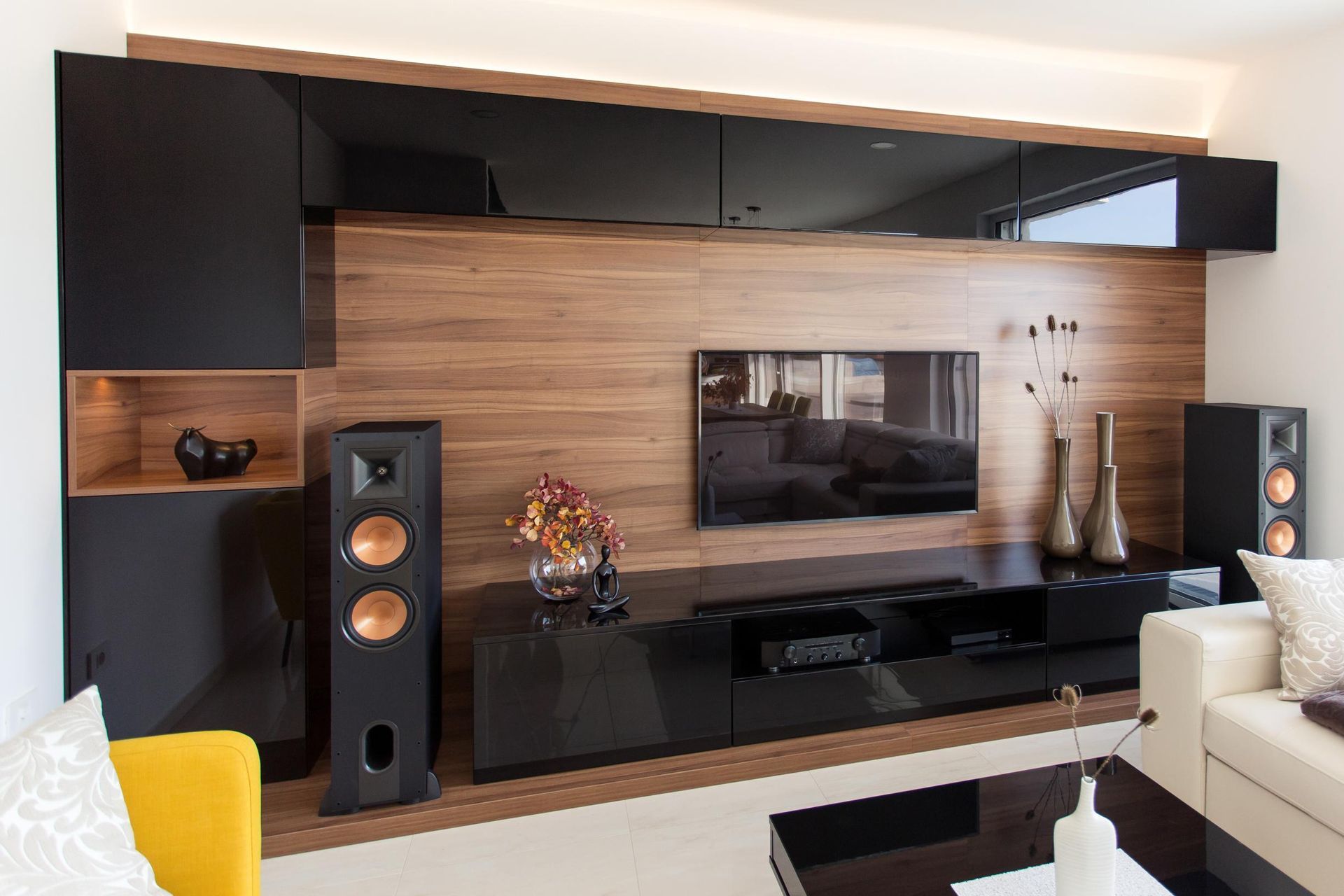 Modern entertainment center: black cabinets, wooden panel, TV, speakers, and decorative vases in a living room.