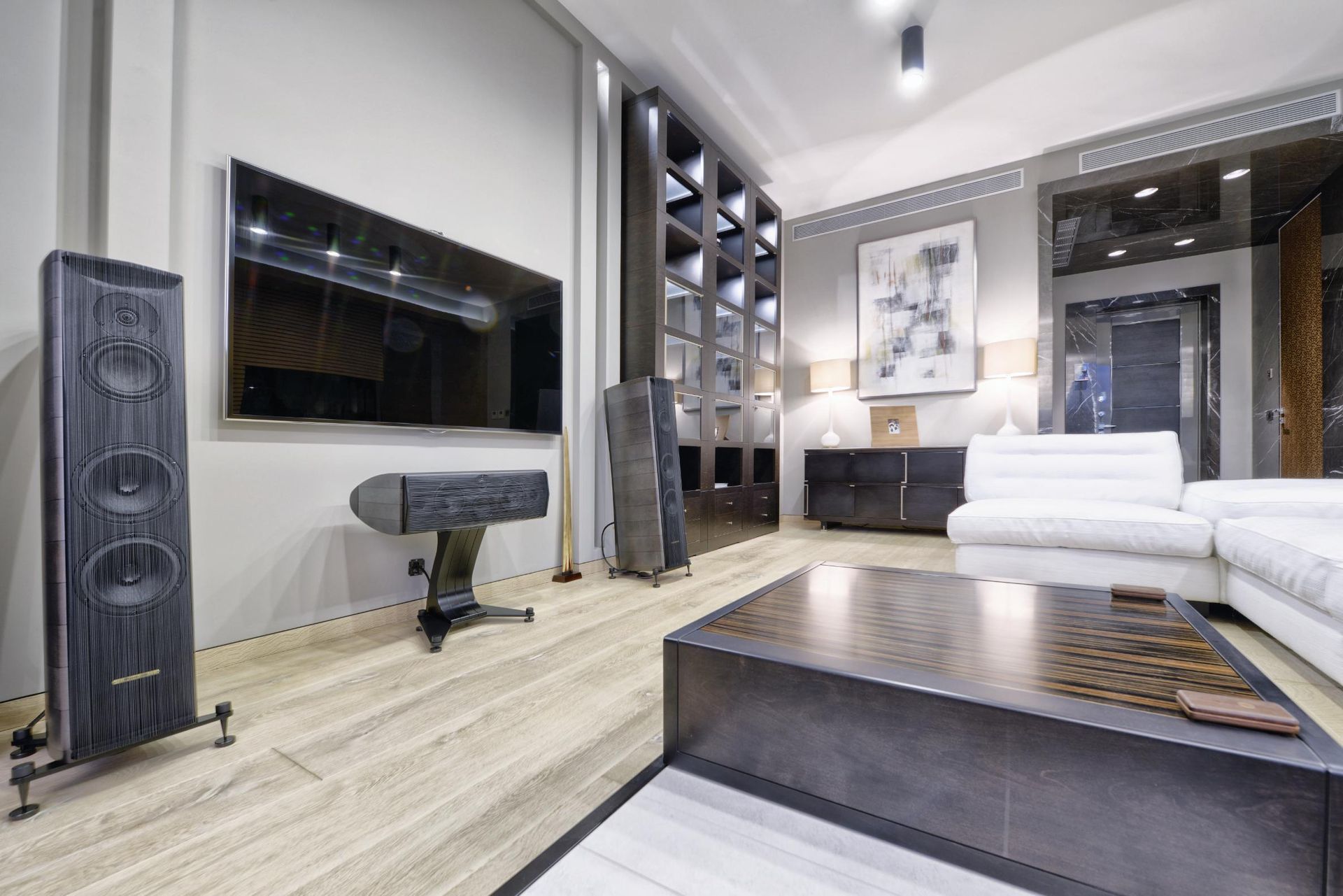 Modern living room with large TV, speakers, leather bench, and a low coffee table.