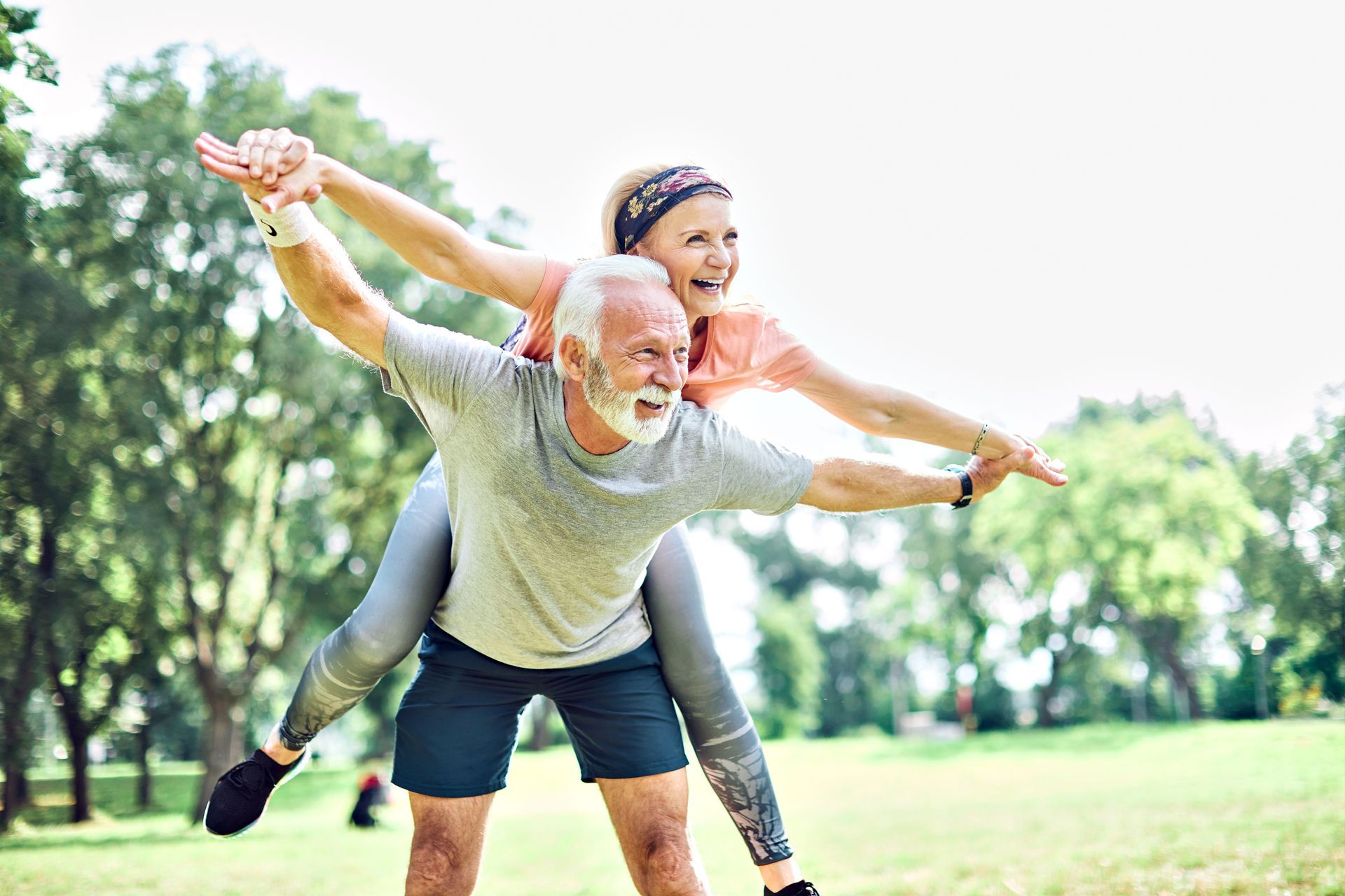 A man is carrying a woman on his back in a park.