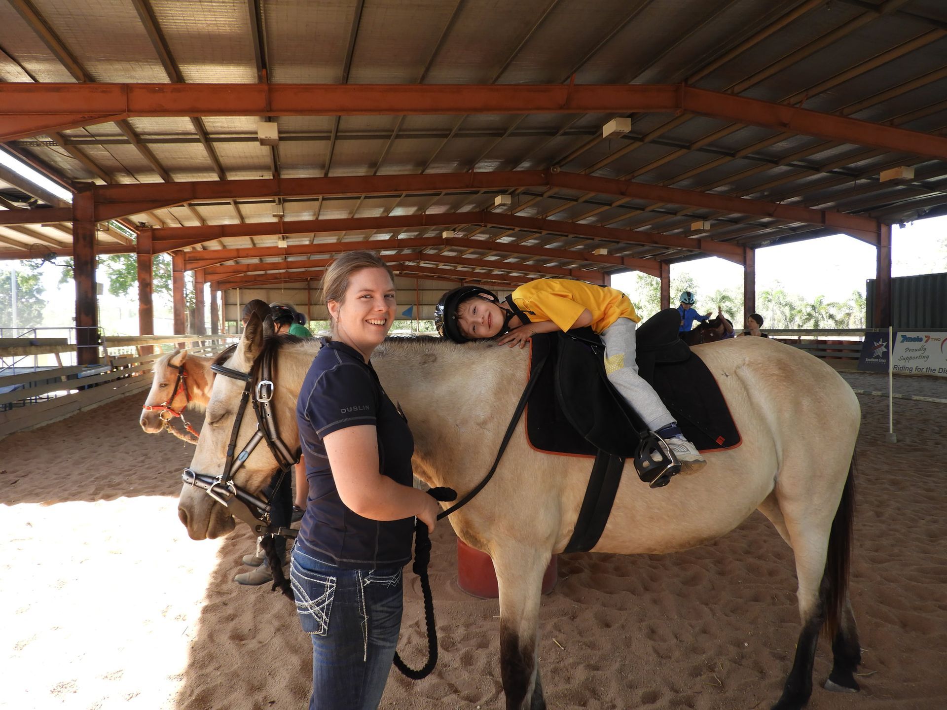 A woman is standing next to a child riding a horse