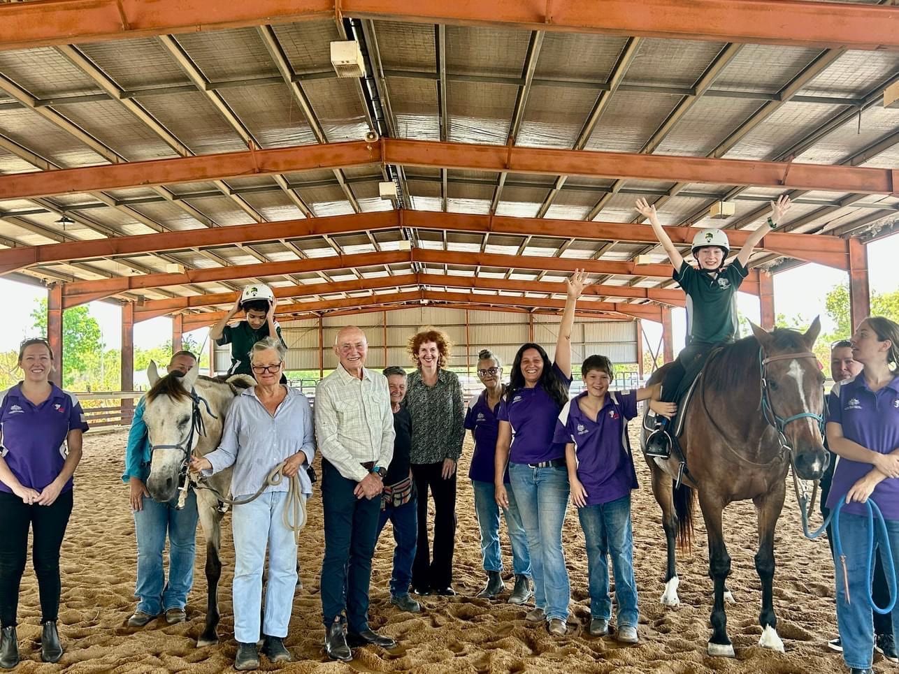 A group of people standing next to horses in a barn.