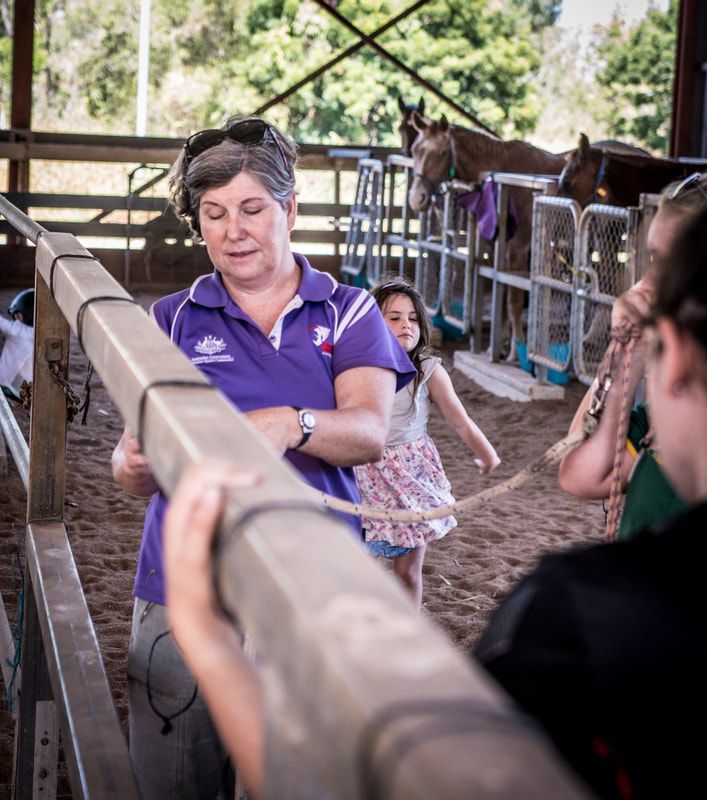 A woman in a purple shirt is standing next to a horse