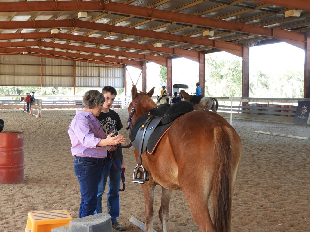 A man and a woman are standing next to a horse in a stable.