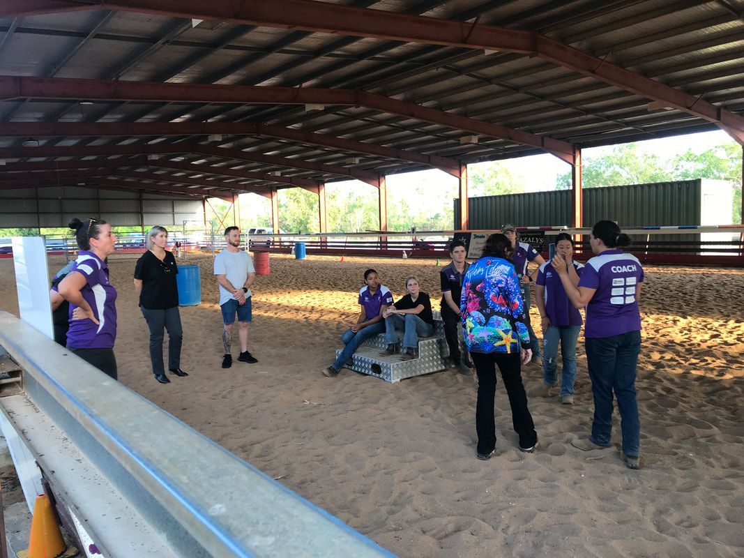 A group of people are standing in a barn talking to each other.