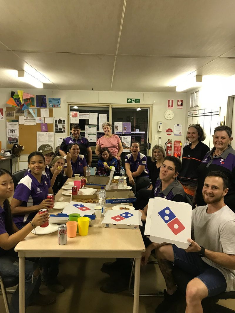 A group of people are sitting around a table holding domino 's pizza boxes.