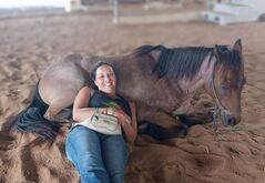 A woman is laying on the ground next to a horse.