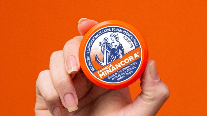 Mão segurando uma pequena caixa de Minancora de cor laranja e azul contra um fundo laranja.