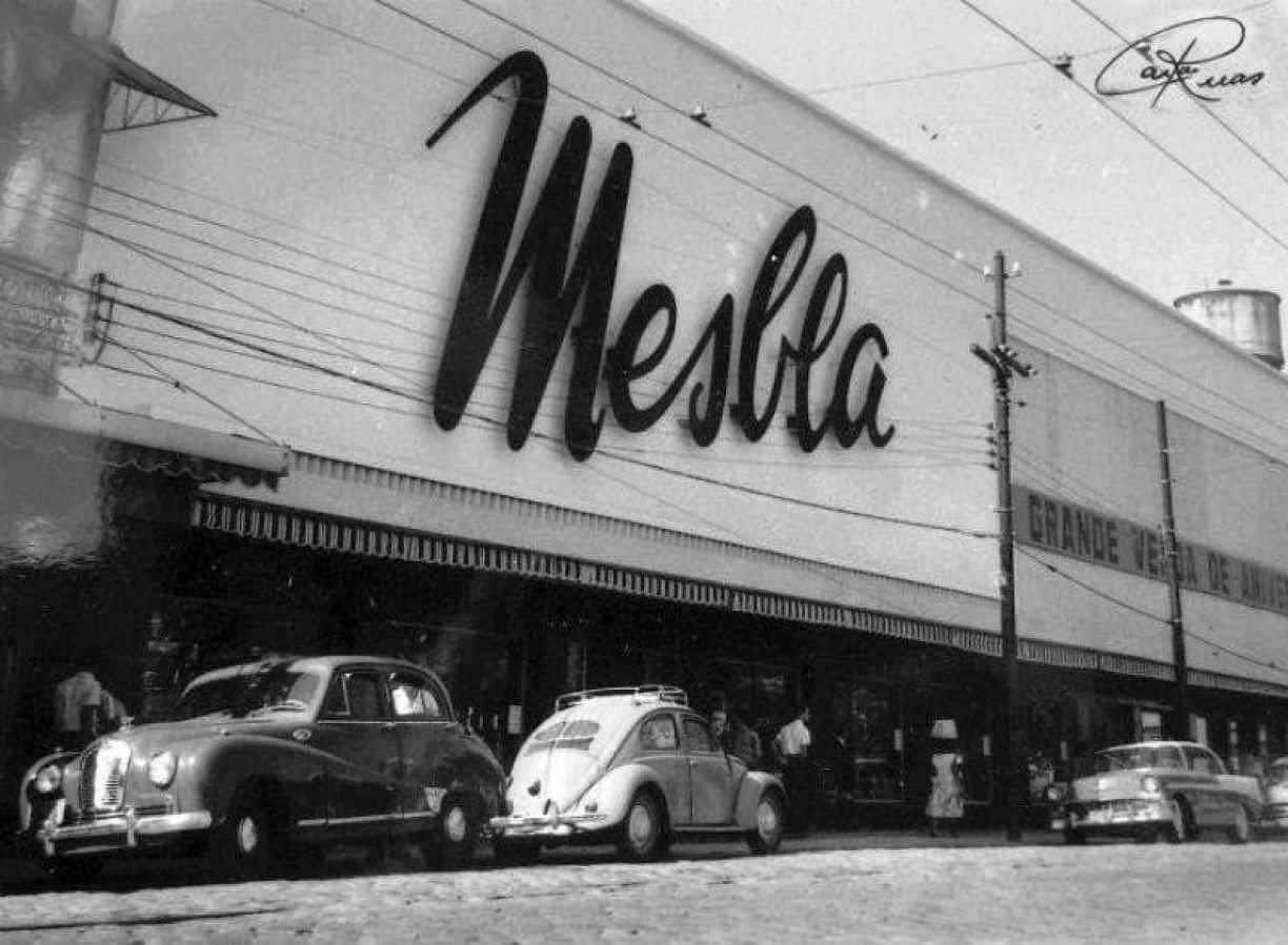 Fotografia em preto e branco de uma loja de departamentos em Mesbla com carros antigos estacionados 