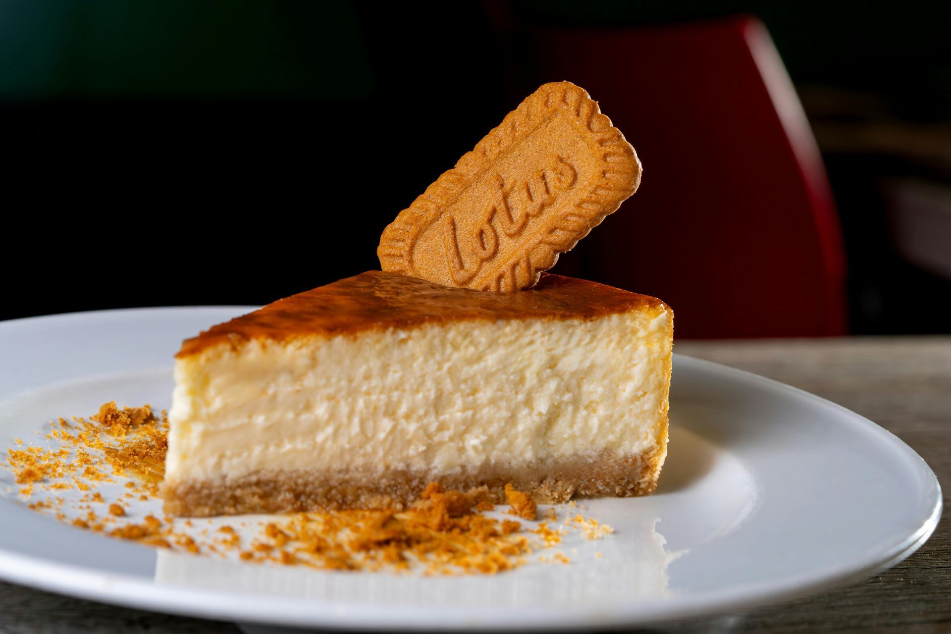 Fatia de cheesecake em um prato branco, decorada com biscoito Biscoff e farofa por cima.