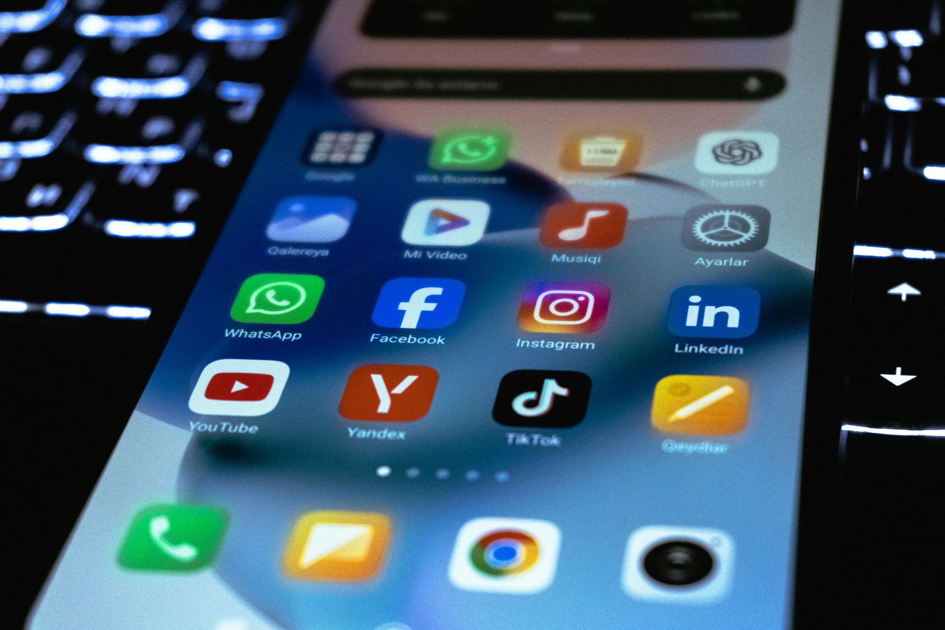 Tela de smartphone exibindo ícones de redes sociais e aplicativos em um teclado de laptop.