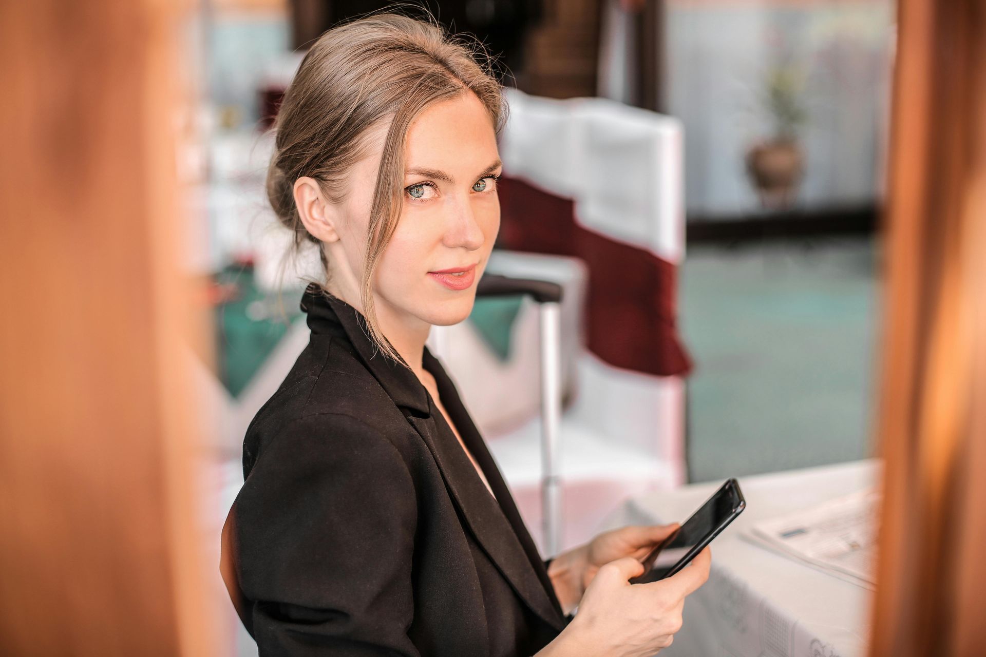 Mulher de blazer preto segurando o telefone, olhando para a câmera, em ambiente interno.
