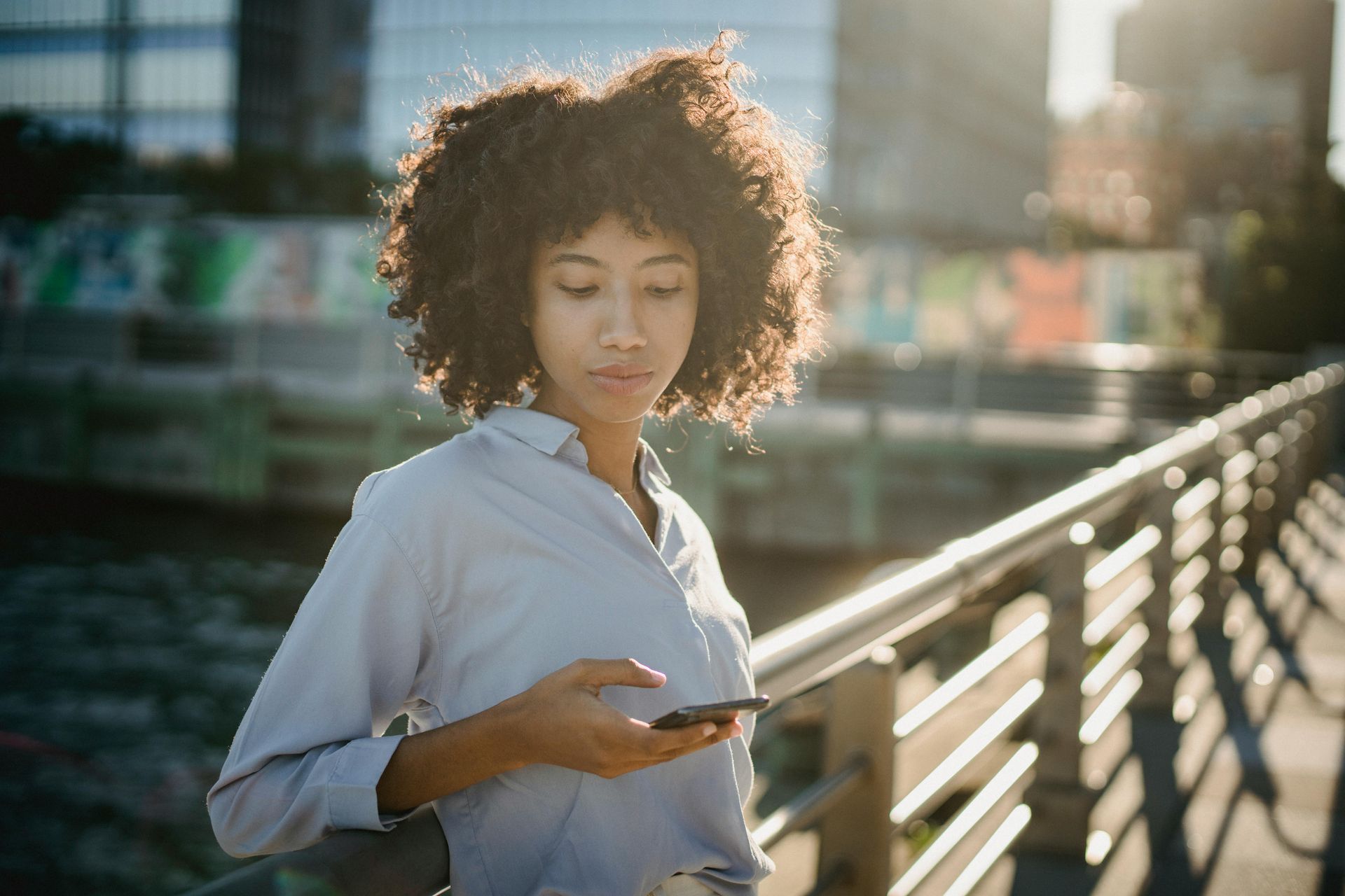 Mulher olhando para um smartphone, em pé ao ar livre em um dia ensolarado.