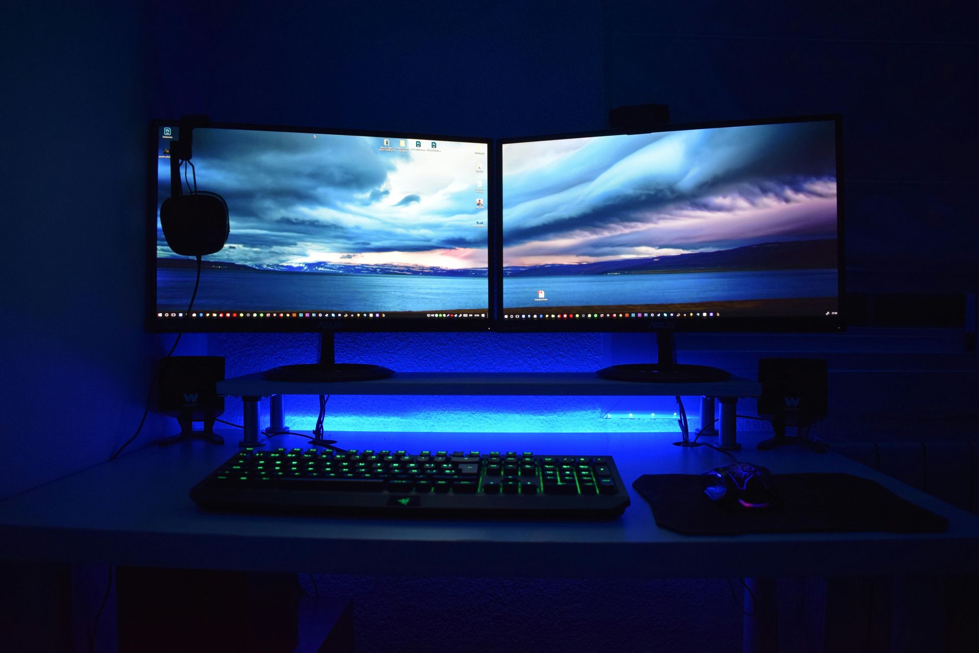 Configuração de jogo com dois monitores curvos, teclado, mouse, alto-falantes e iluminação LED azul