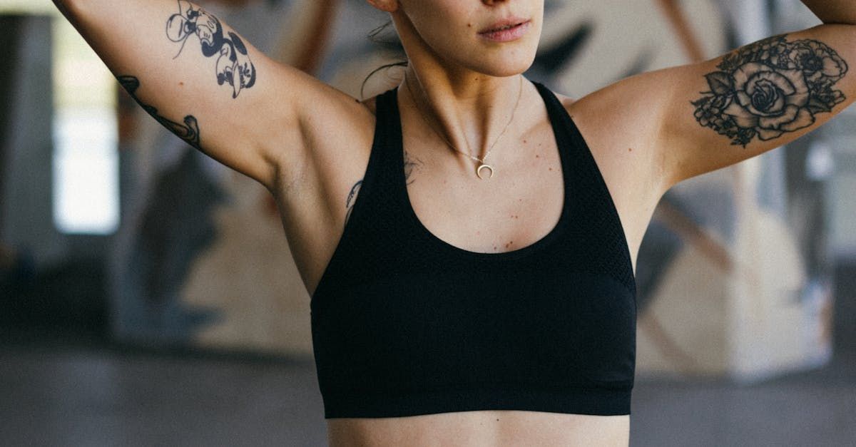 A woman with tattoos on her arms and chest is wearing a black sports bra.