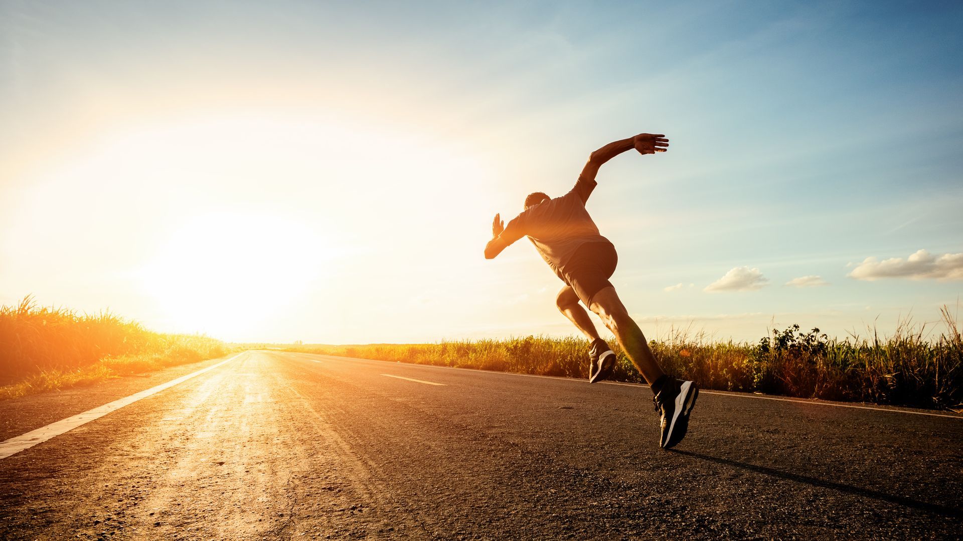 A man is running down a road at sunset.