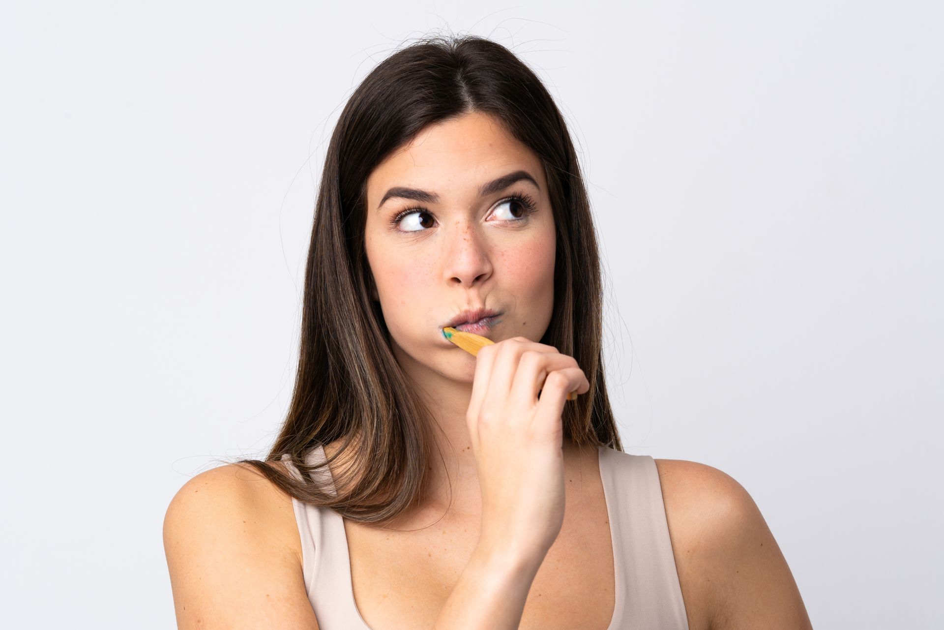 A woman is brushing her teeth with a toothbrush and looking up.