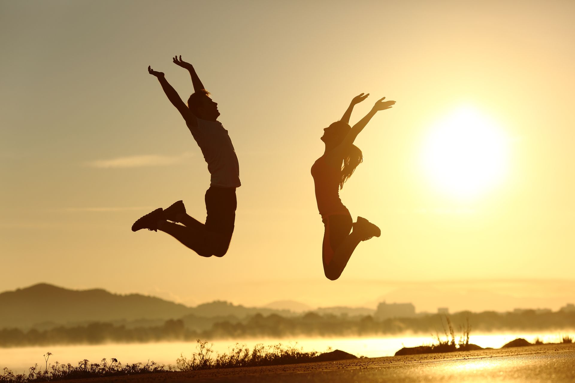 Two people are jumping in the air at sunset