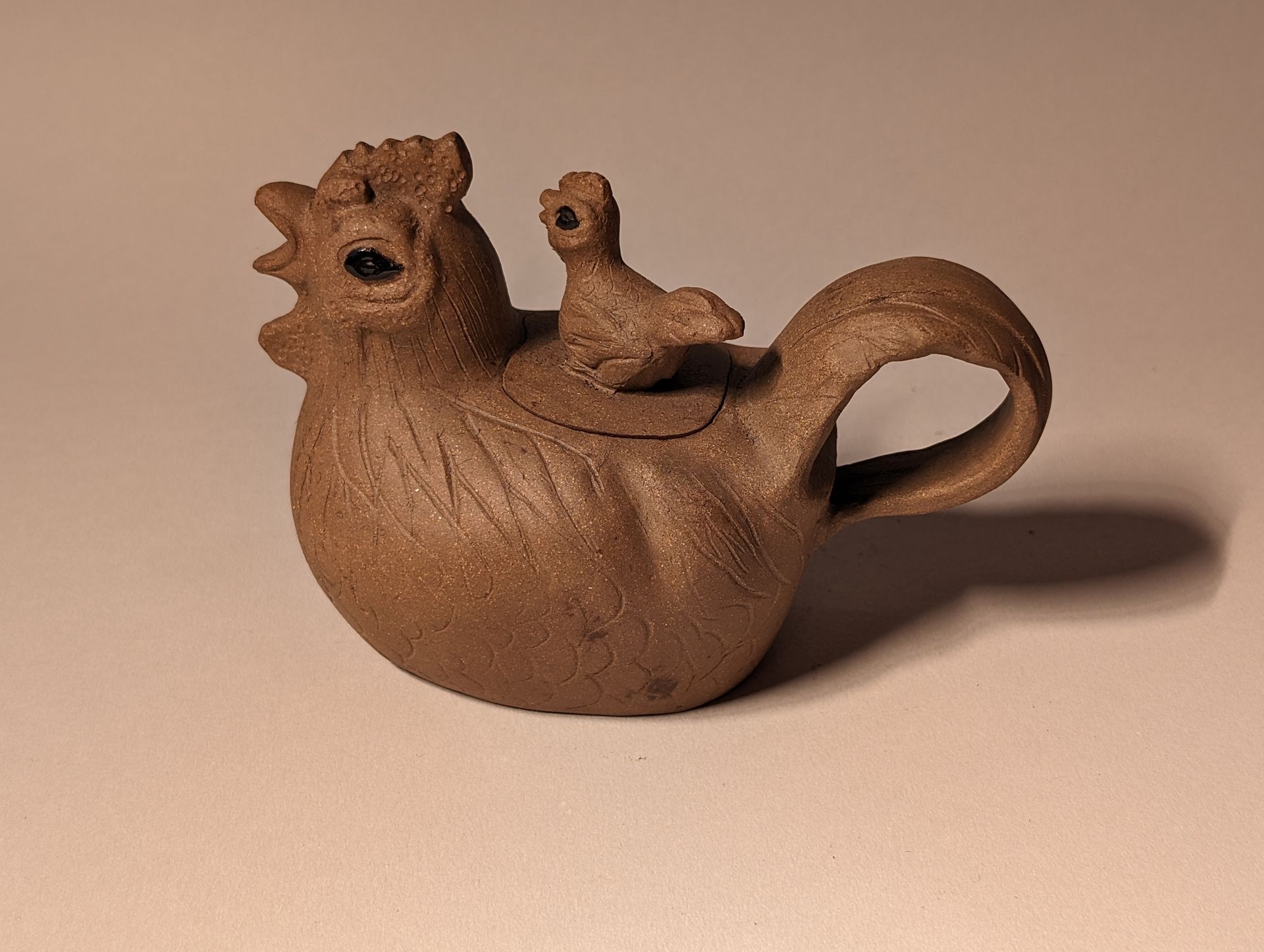 A brown chicken shaped teapot with a smaller chicken on its back