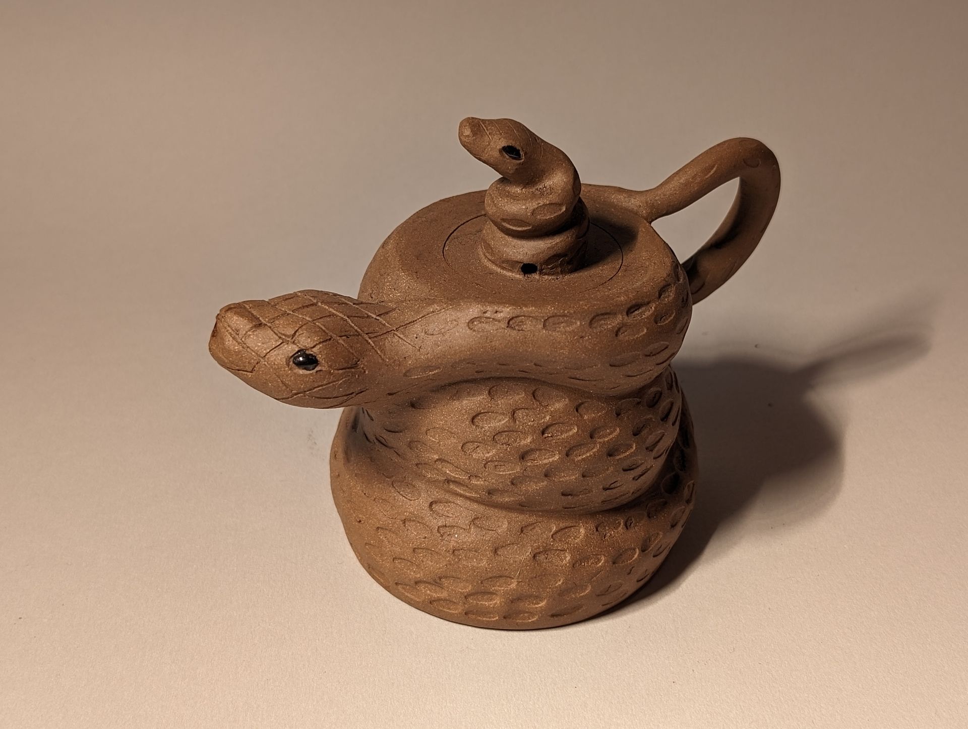 A brown teapot with a snake on top of it