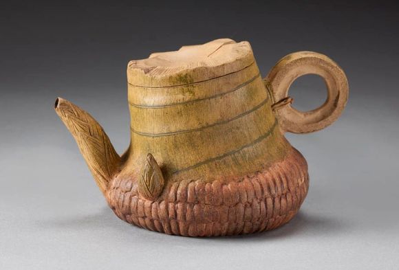Rustic handmade clay teapot with a tan lid and brown textured base on a gray background