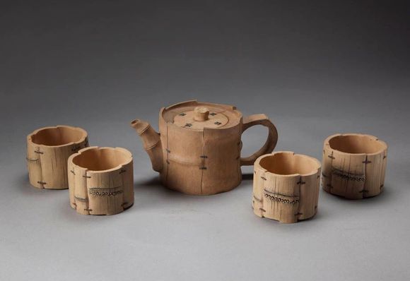 Five small clay cups and a teapot with lid on a gray background