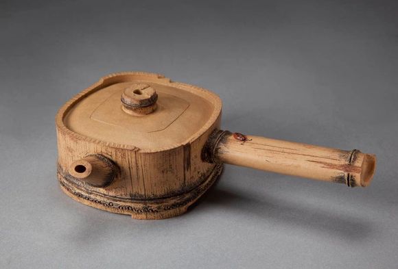 Wooden hand-carved pot with lid and side handle on a gray background