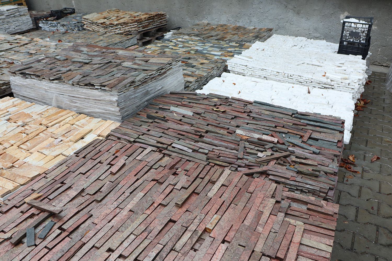 Stacks of stone pavers sorted by color and size at an outdoor landscaping supply yard.