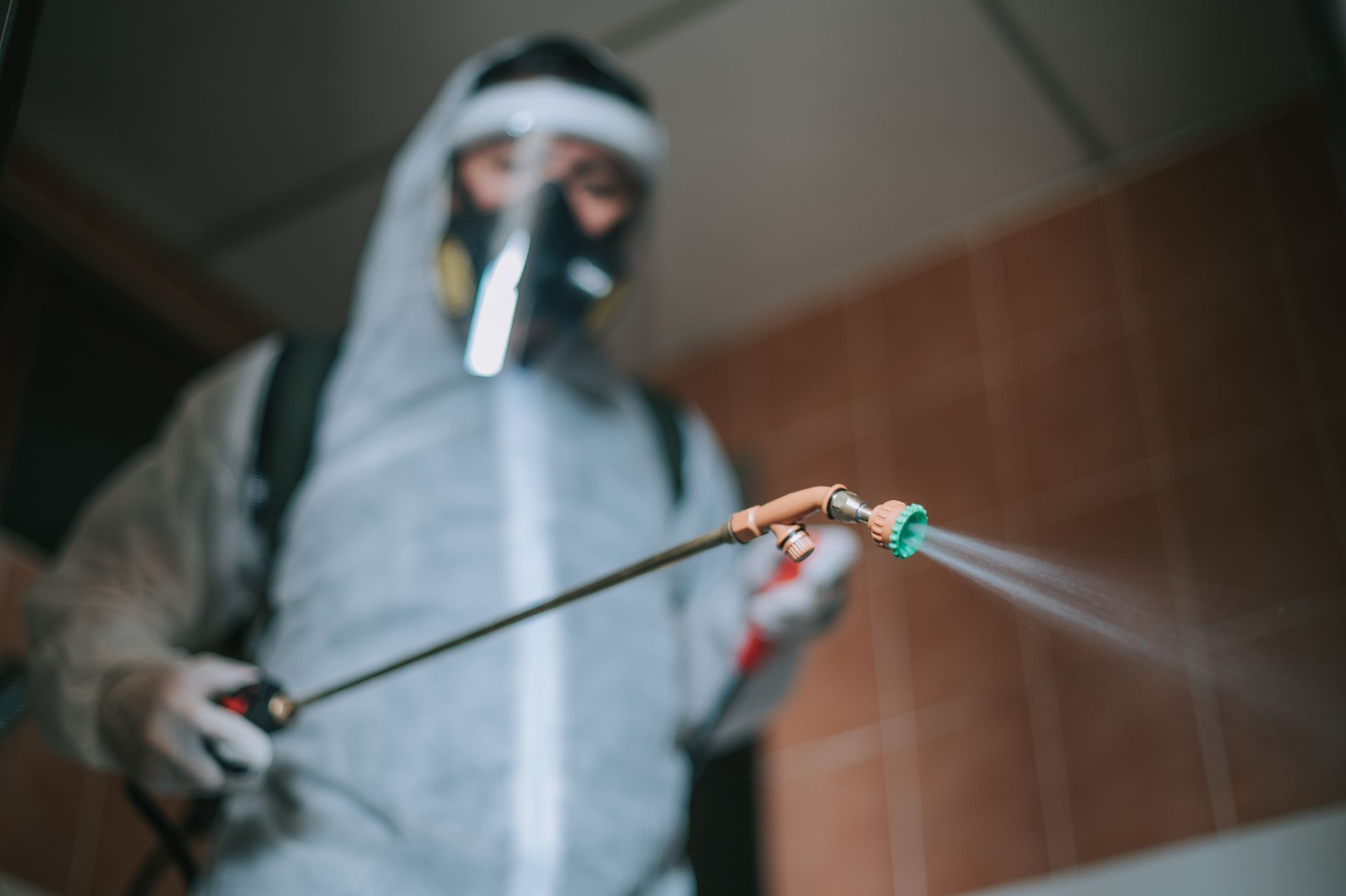 Un uomo con una tuta protettiva sta spruzzando una stanza con uno spruzzatore.