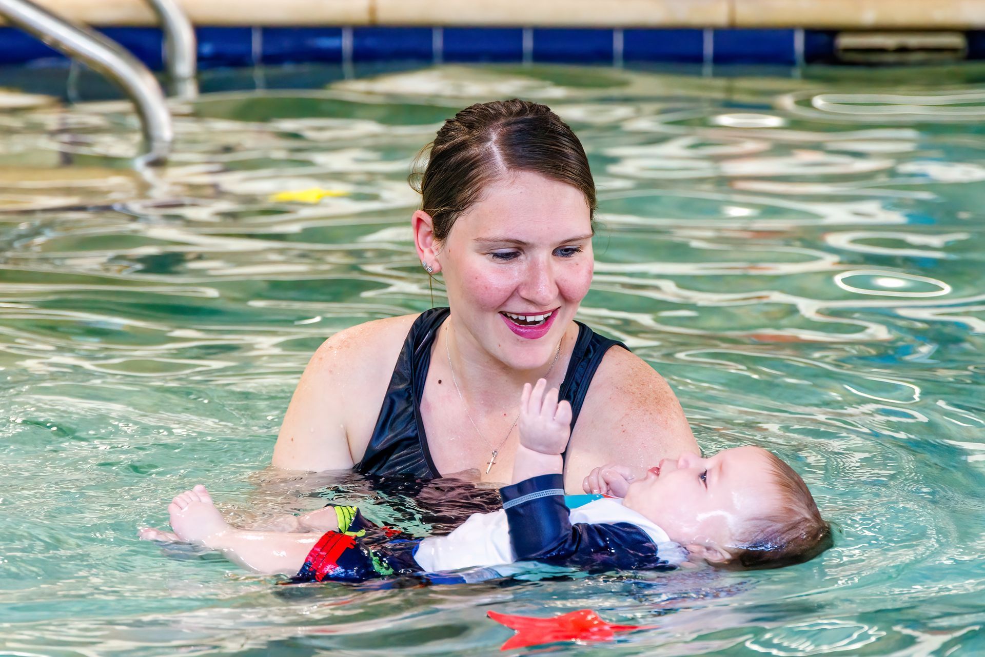 Woman in swimsuit smiling at baby floating in a pool.