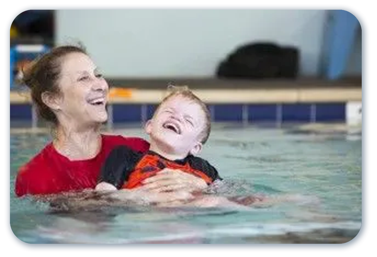 Woman and child laughing in a pool. Woman wears red shirt and holds the child wearing a black and orange rash guard.