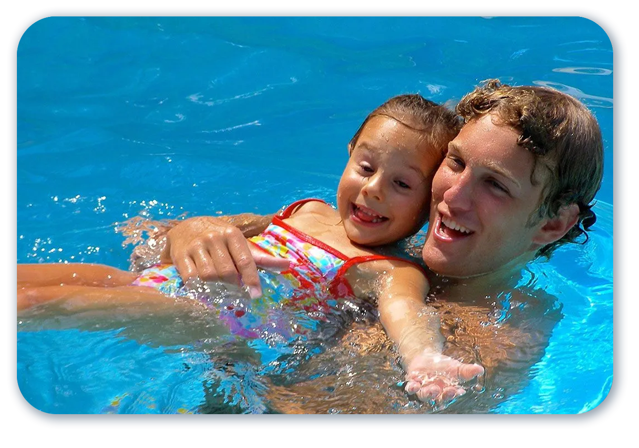 Man in pool holding a smiling girl; both are enjoying the water.