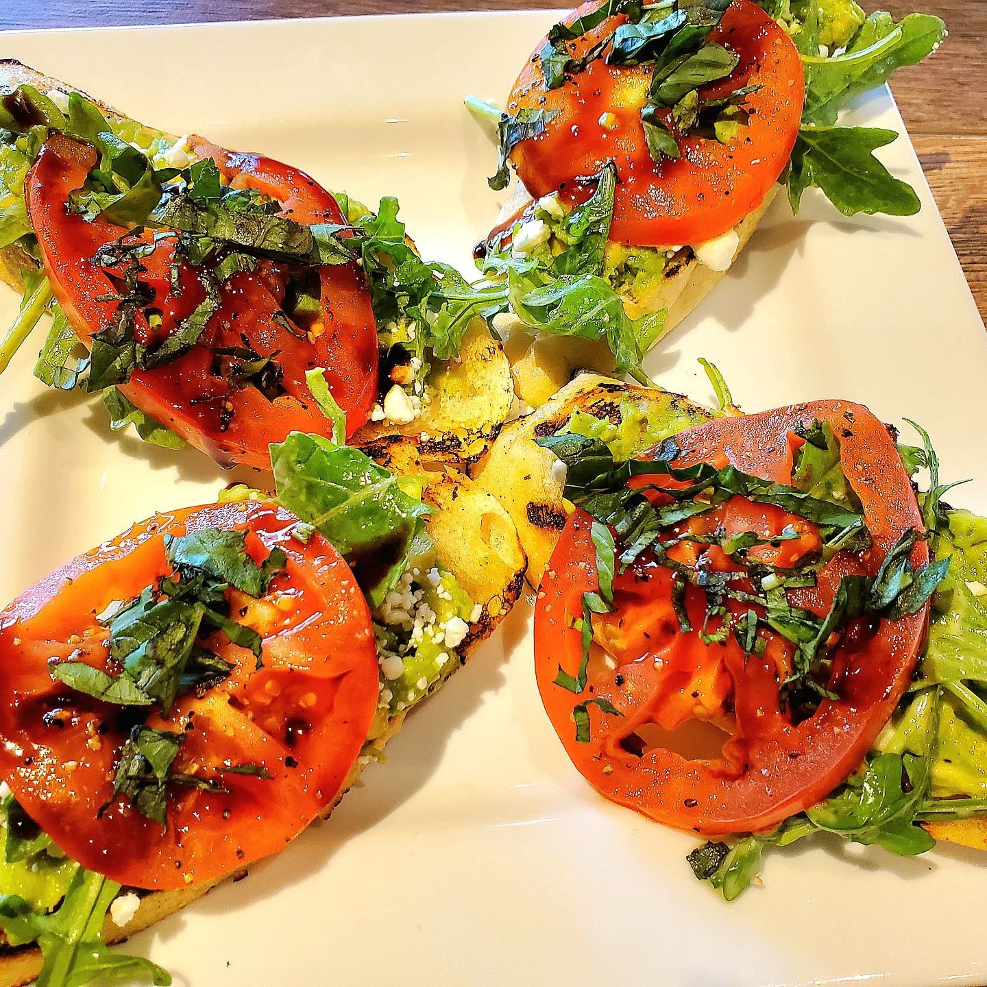 Bruschetta with grilled tomato slices, arugula, and basil on a white plate.