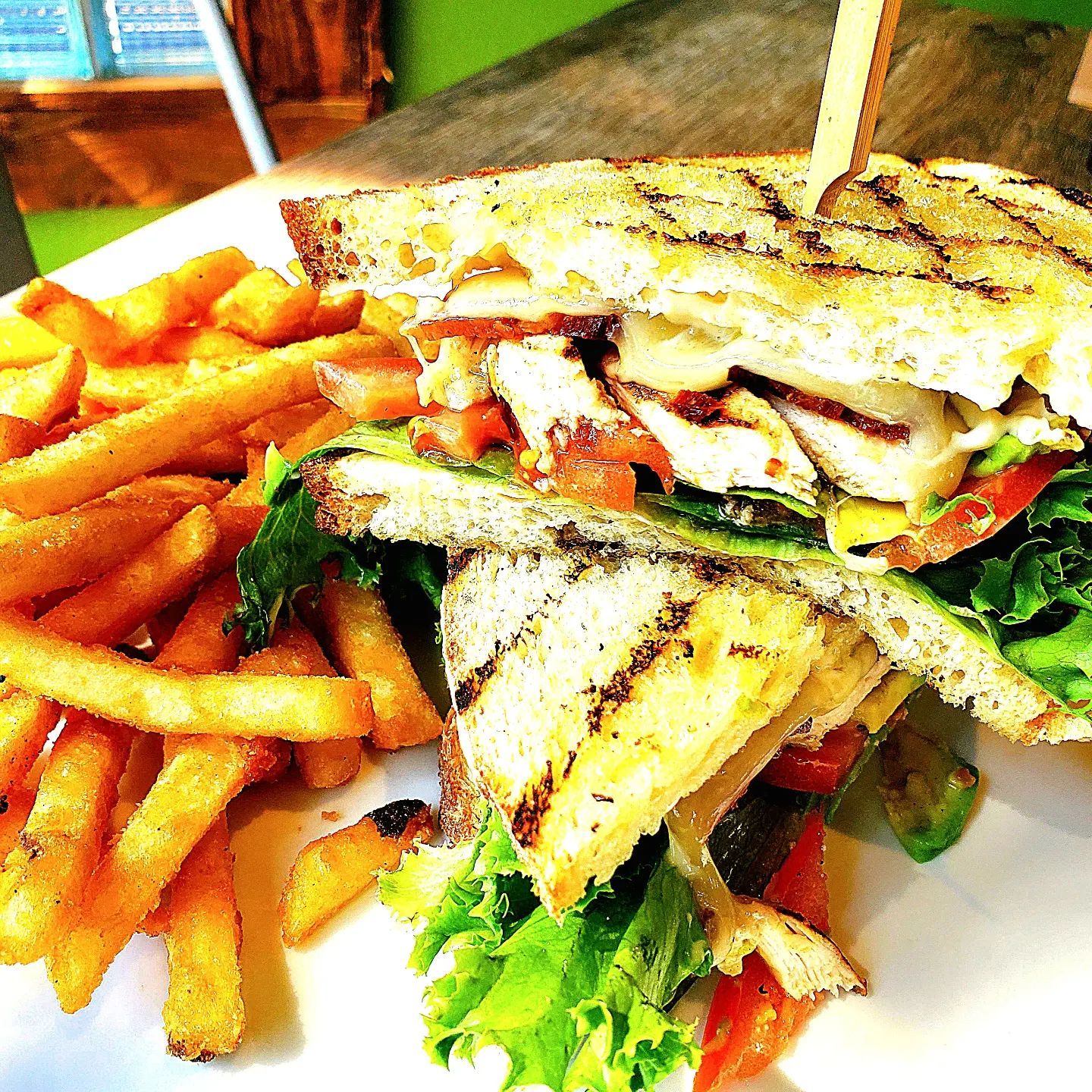 Grilled chicken sandwich with fries on a white plate.