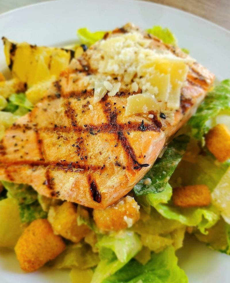 Grilled salmon fillet atop Caesar salad, with croutons and shaved Parmesan.