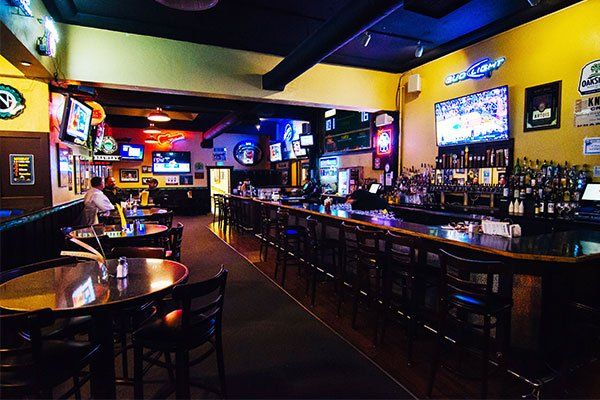 Interior of a sports bar with a long bar, tables, and multiple TVs displaying sports games.