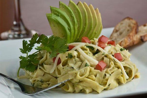 Pasta salad with avocado, tomatoes, cilantro, and sliced avocado garnish on a white plate.