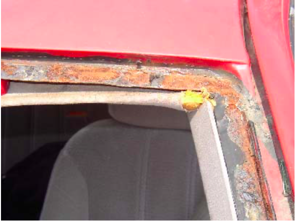 A close up of a rusty window frame on a red car