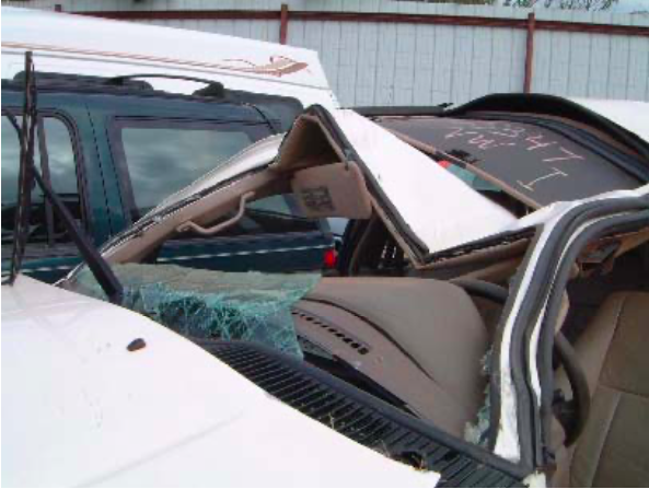 A white car with a broken windshield is sitting in a junkyard