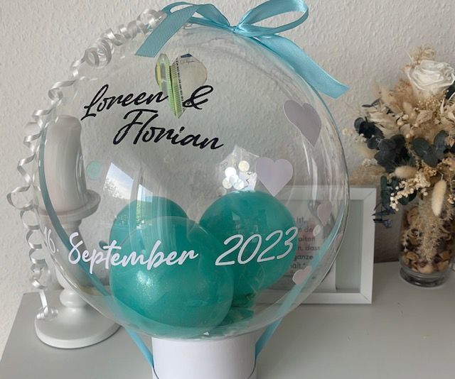 Durchsichtiger Ballon mit türkisfarbenen Ballons im Inneren, darauf die Namen „Loreen & Florian“ und „September 2023“.