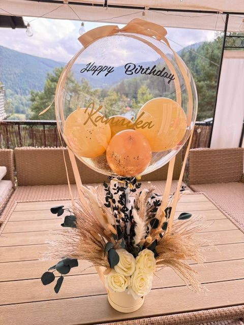 Ein Heißluftballon gefüllt mit gelben Ballons und Blumen auf einem Tisch.