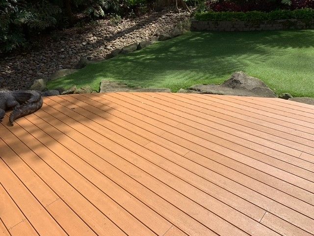 A dog is laying on a wooden deck in a backyard.