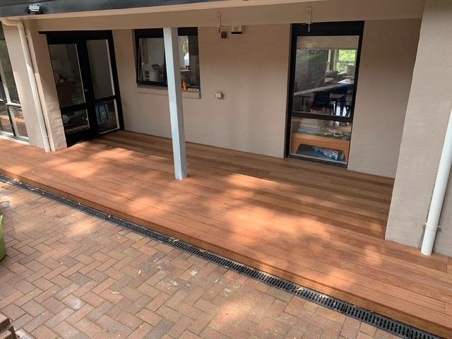 A wooden deck is sitting under a covered porch in front of a house.