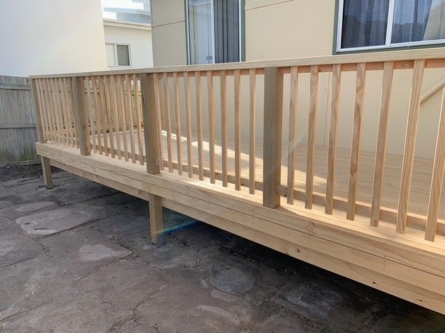 A wooden deck with a railing is sitting in front of a house.