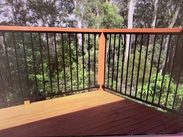 A wooden deck with a metal railing and trees in the background