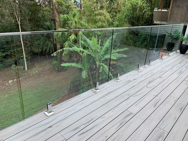 A wooden deck with a glass railing and trees in the background.